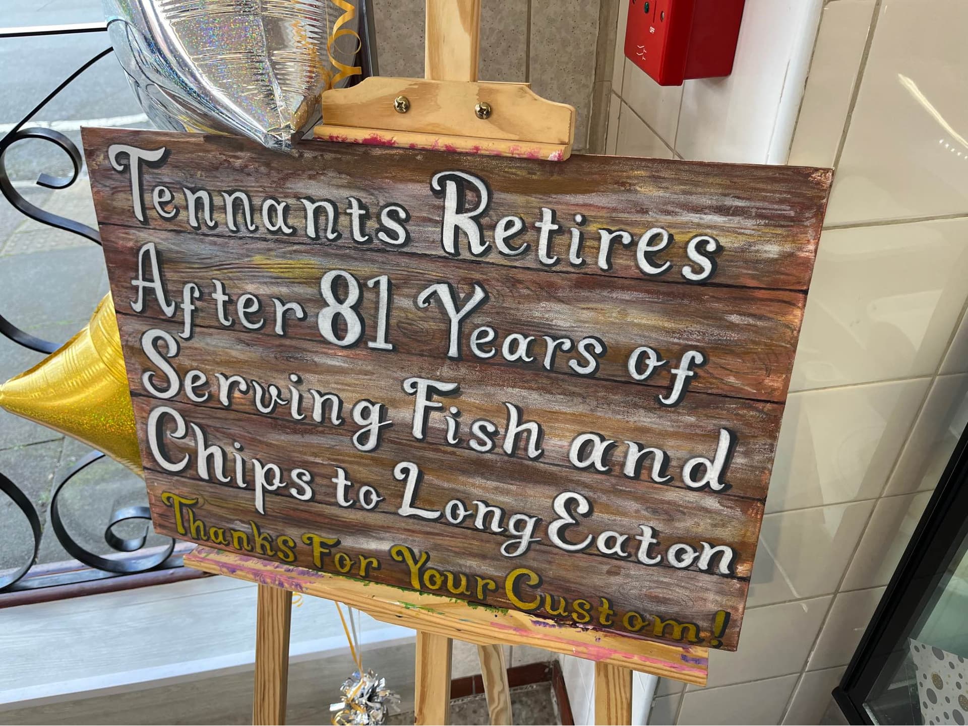 A painted sign stating 'Tennants Retires After 81 Years of Serving Fish and Chips to Long Eaton. Thanks For Your Custom!'.